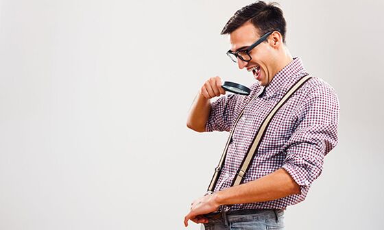 A man looks through a magnifying glass at his penis, wanting to increase its size